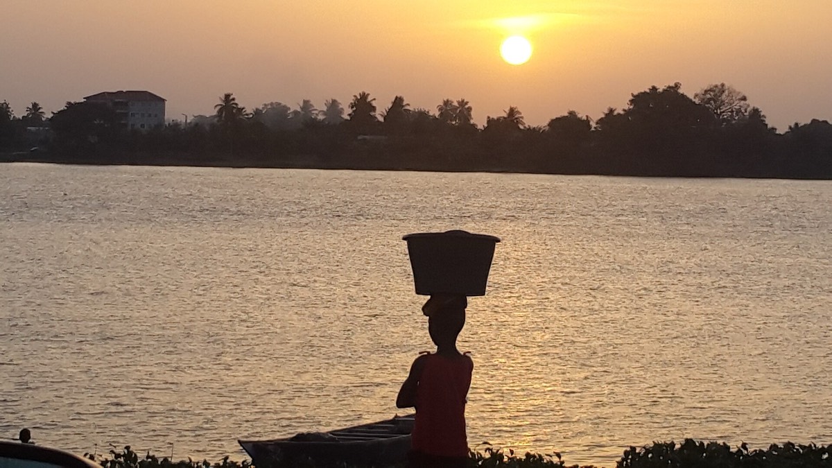 A woman carrying a basin on her head, silhouetted against the sunset over the Lower Volta